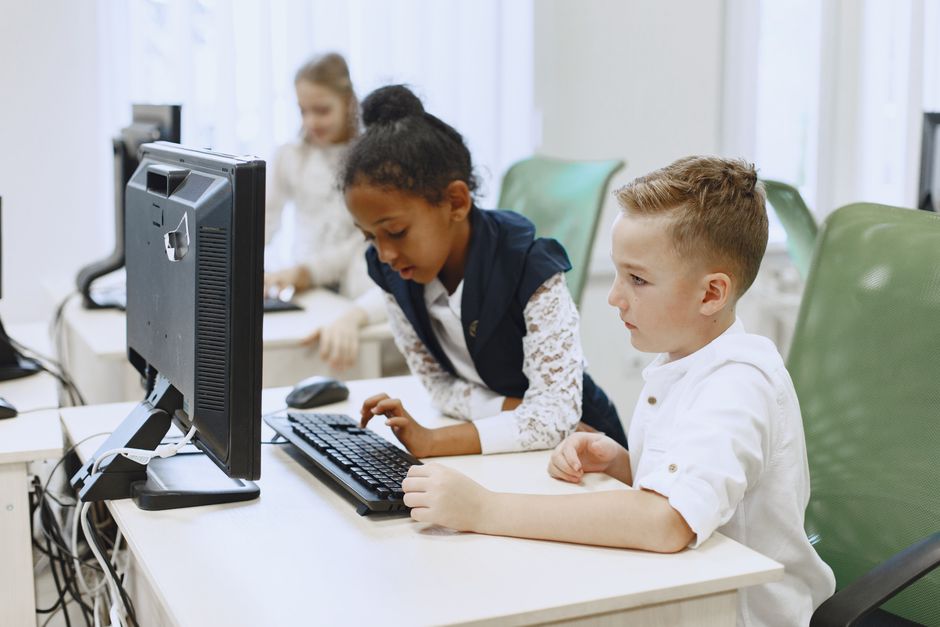 Diverse children working together on computers in a modern school setting.