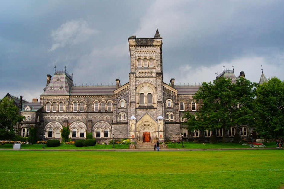 Stunning Gothic Revival building amidst lush greenery under a cloudy sky in Toronto.