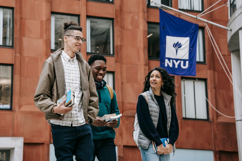 Low angle of cheerful multiethnic classmates in casual clothes with notebooks talking while standing near university