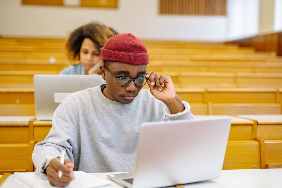 Young adults studying in a university lecture hall with laptops, focused on coursework.