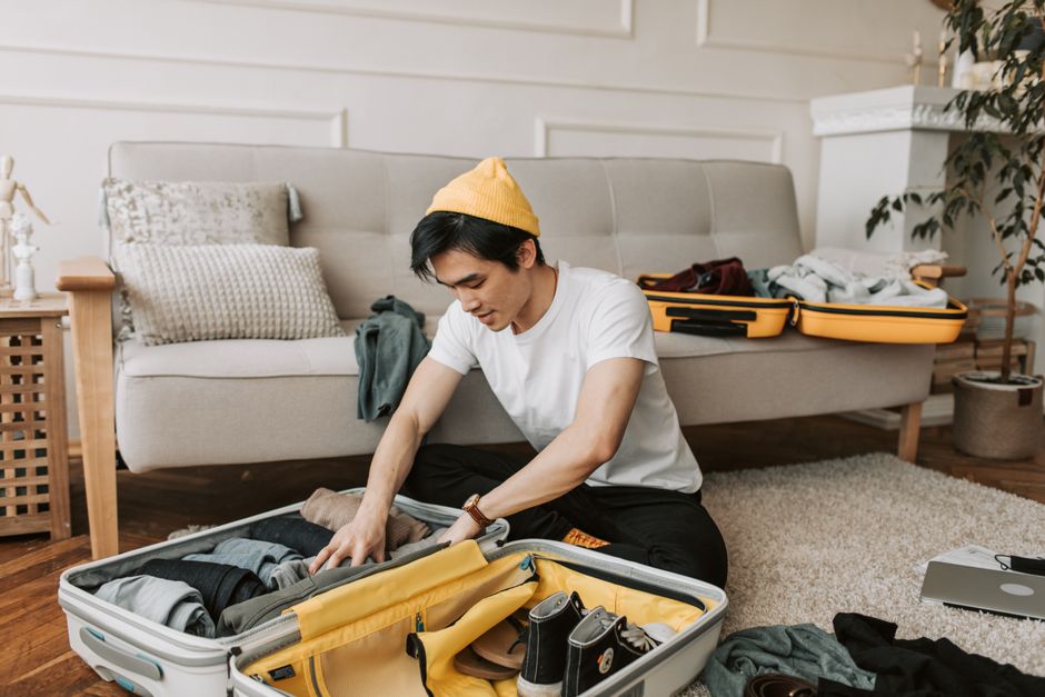 Young man organizing clothes in a suitcase in a cozy living room, preparing for travel.