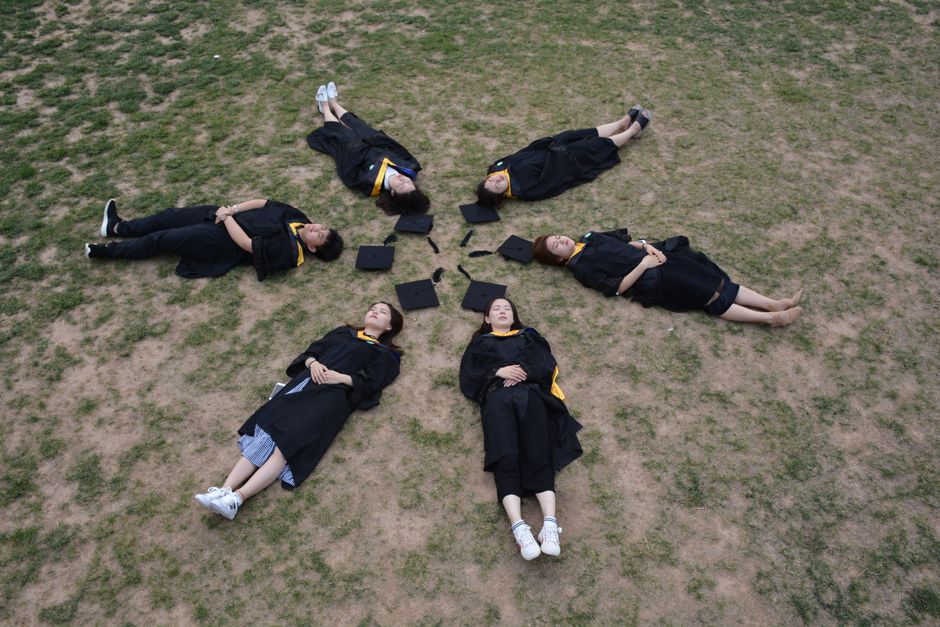 Aerial photo of six graduates lying in a star shape on grass.