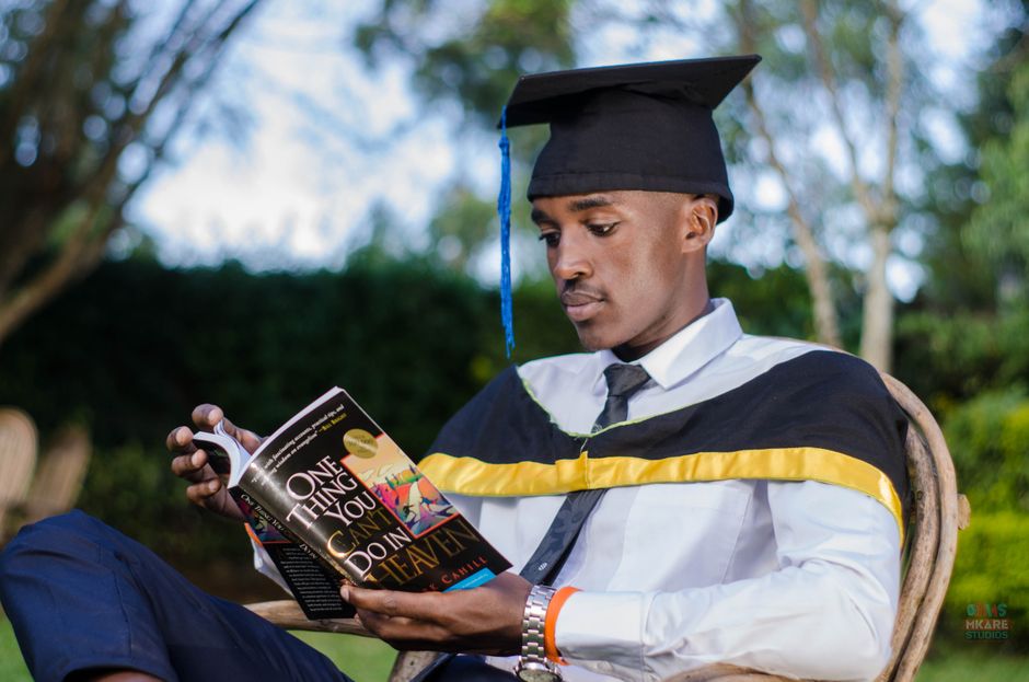 A young graduate in cap and gown reading outdoors, symbolizes education and accomplishment.