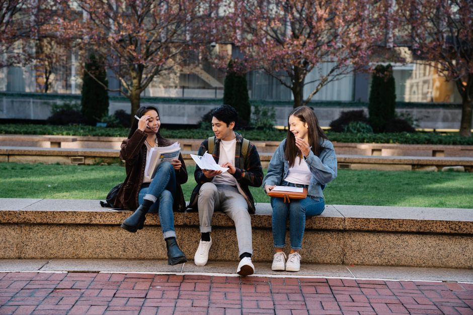 Group of college students laughing and studying outdoors on a campus bench during spring.