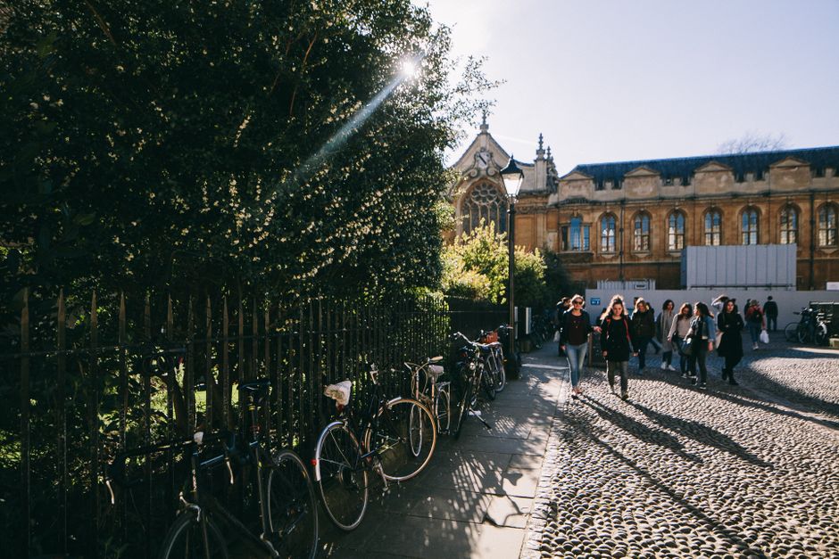 Sunlit street with bikes, people walking by a historical university building.